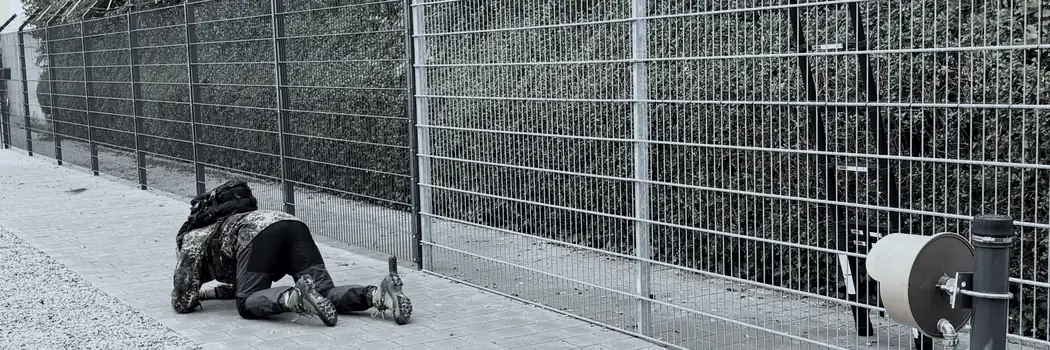 Übung auf dem Testgelände: Person in Tarnkleidung kriecht auf dem Weg am Doppelstabmattenzaun entlang – Test- und Schulungsgelände, Eggenfelden.